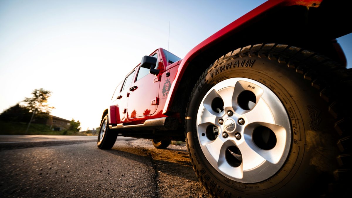 Red all-terrain vehicle showcasing all-wheel drive capabilities, emphasizing the tire and wheel design, set against a sunset backdrop.